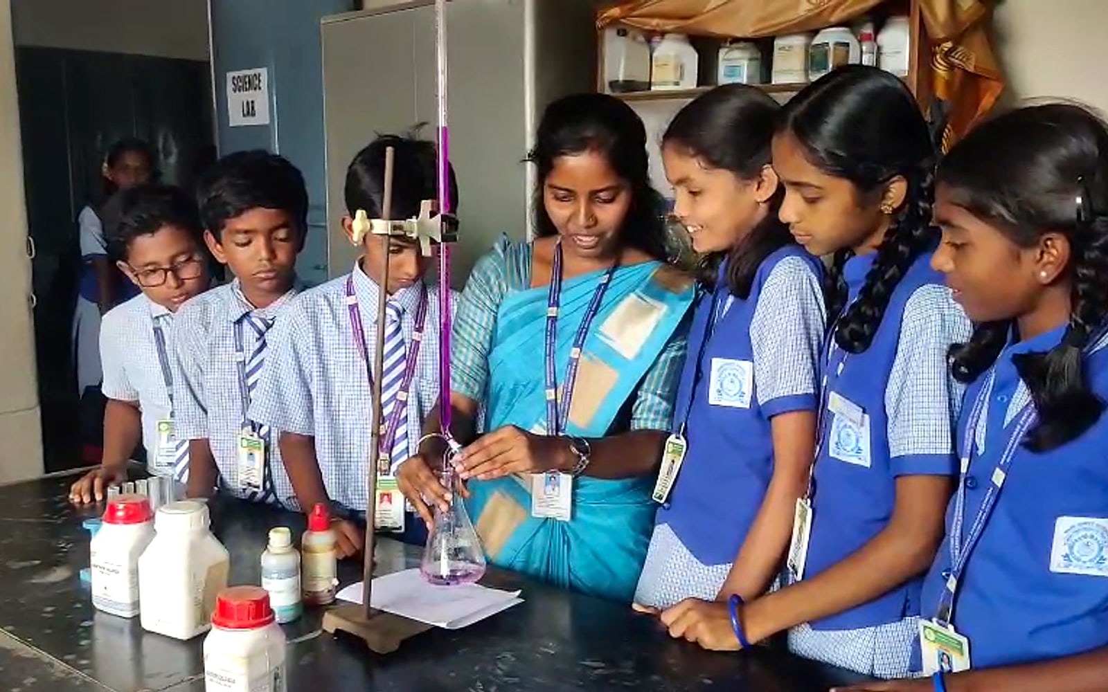 Science teacher demonstrating a titration experiment with a burette and conical flask to Manjushree students in the school science lab